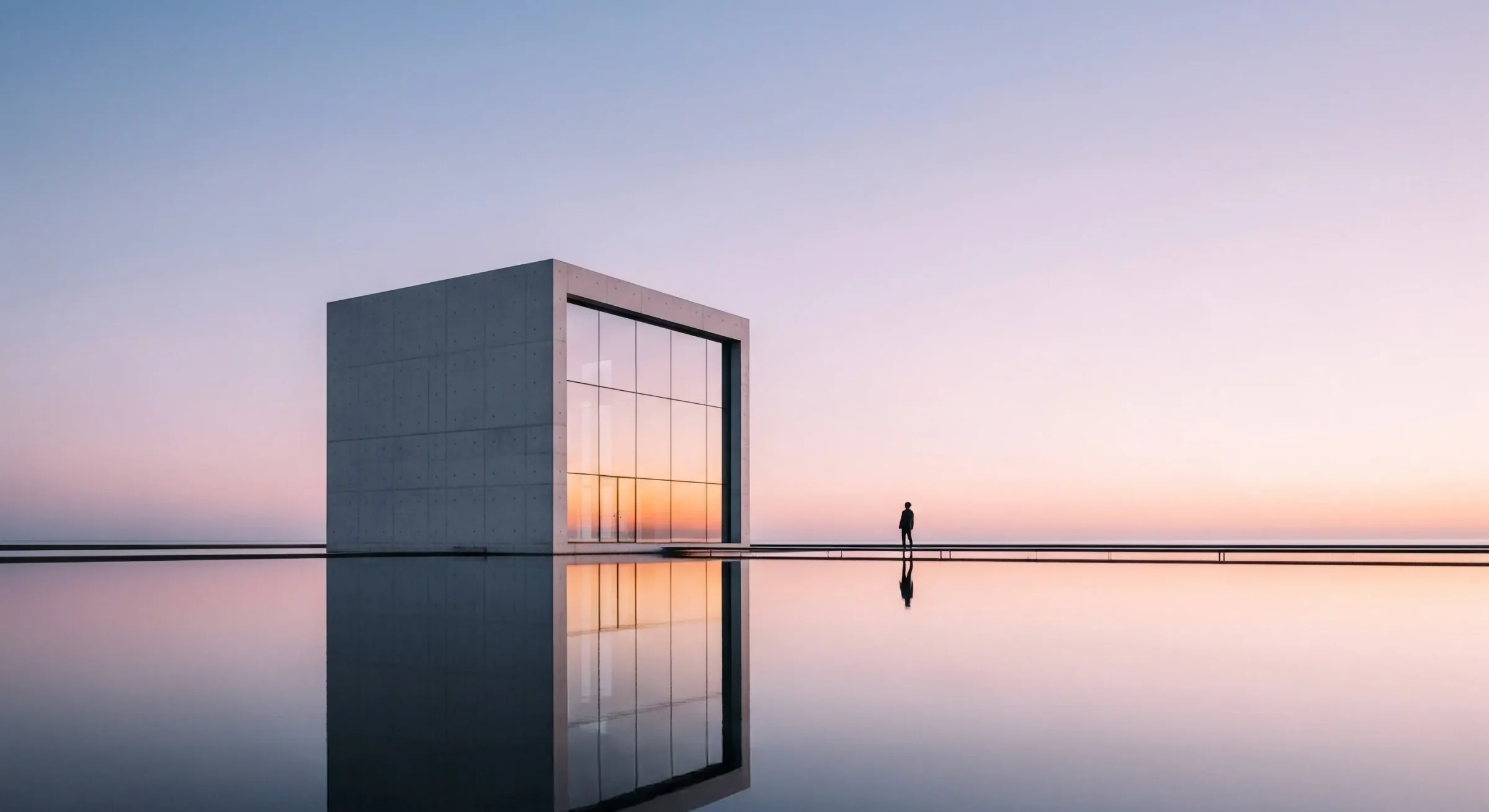 Monolithic concrete pavilion with a tall glazed opening reflected in still water at dusk.